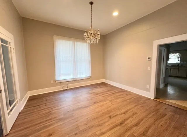 an empty room with wooden floor chandelier and windows