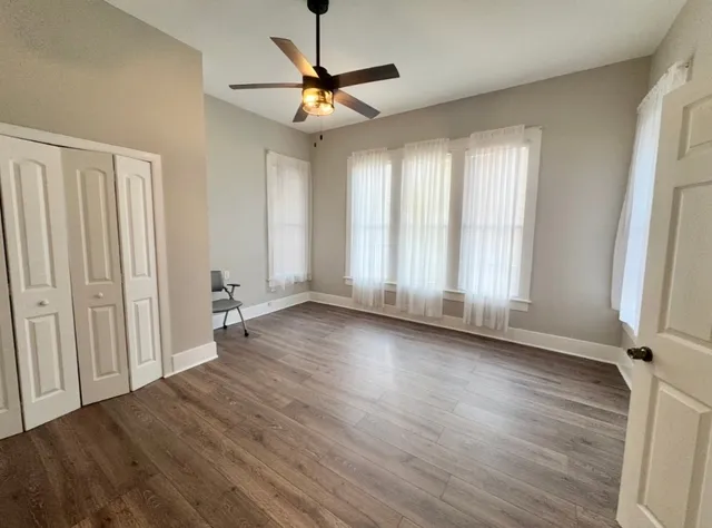 an empty room with wooden floor fan and windows