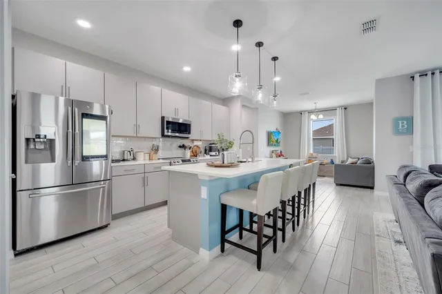 a kitchen with stainless steel appliances a refrigerator a stove a sink a dining table and chairs with wooden floor