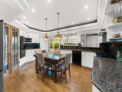 a kitchen with stainless steel appliances granite countertop a stove a refrigerator a kitchen island a dining table and chairs with wooden floor