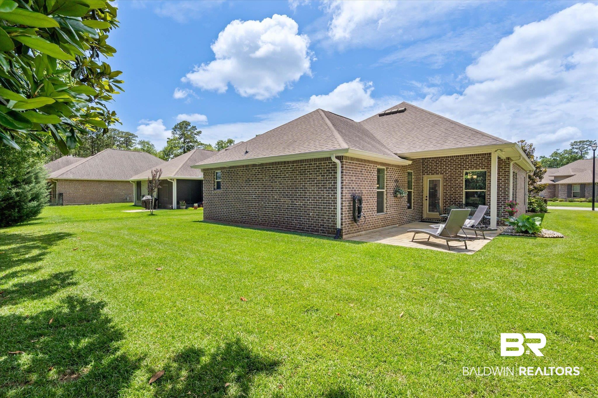 1270 Surrey Loop Foley, AL 36535 - Photo 24 of 27 Expansive green lawn surrounds a brick exterior home featuring a concrete patio, covered porch area, and a rear entry door with window