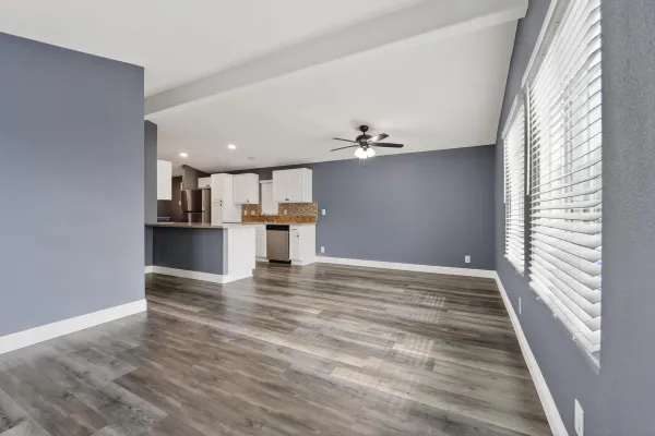 a view of empty room with wooden floor and kitchen view