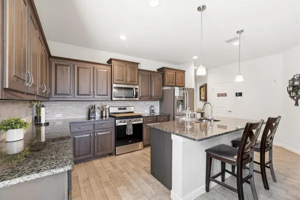 a kitchen with stainless steel appliances granite countertop a stove top oven a sink dishwasher a dining table and chairs with wooden floor