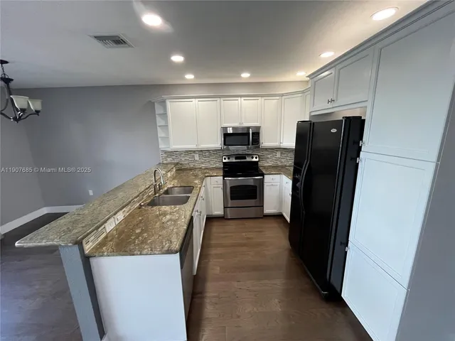 a kitchen with stainless steel appliances granite countertop a stove and a view of living room