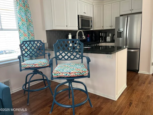 a kitchen with stainless steel appliances kitchen island granite countertop a refrigerator a stove a sink a dining table and chairs with wooden floor