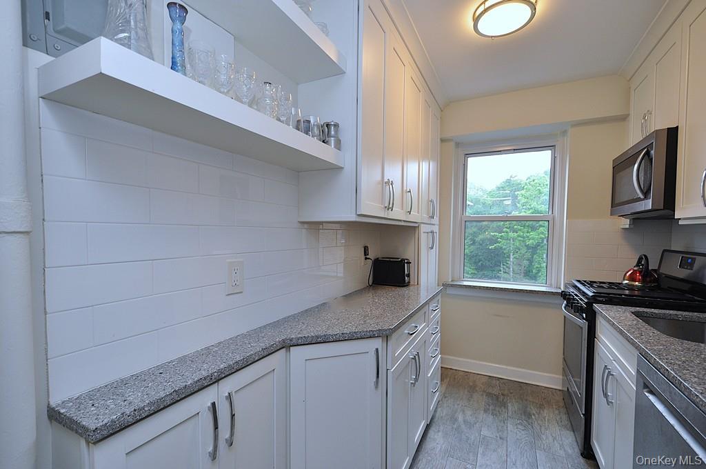 235 Garth Road, Unit A5B Scarsdale, NY 10583 - Photo 8 of 47 a kitchen with granite countertop a sink a stove a microwave and wooden cabinets