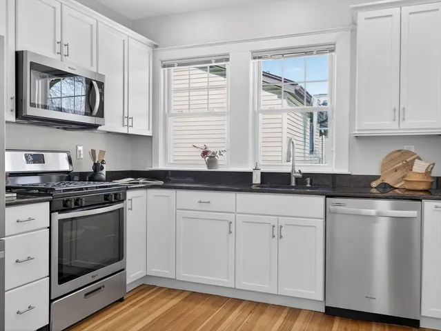 a kitchen with stainless steel appliances granite countertop white cabinets a sink a stove a window and white wooden cabinets