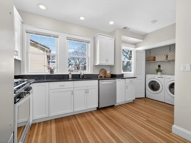 a large white kitchen with a stove a sink and dishwasher with wooden floor