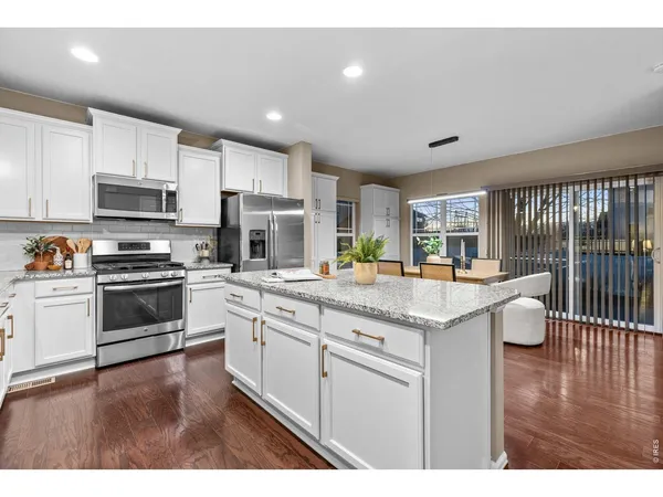a kitchen with stainless steel appliances granite countertop a refrigerator a sink dishwasher a stove and white cabinets with wooden floor