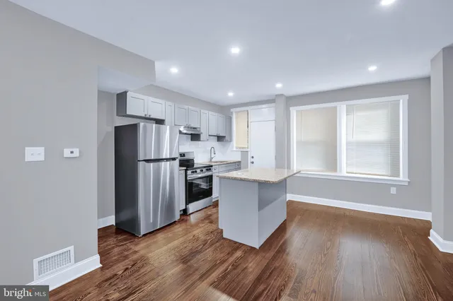 a kitchen with stainless steel appliances granite countertop a refrigerator a sink dishwasher a stove and white countertops with wooden floor