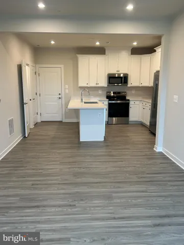 a large kitchen with kitchen island a stove a sink a refrigerator white cabinets and wooden floor