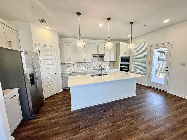 a large kitchen with a refrigerator a sink dishwasher a oven and a dining table with wooden floor