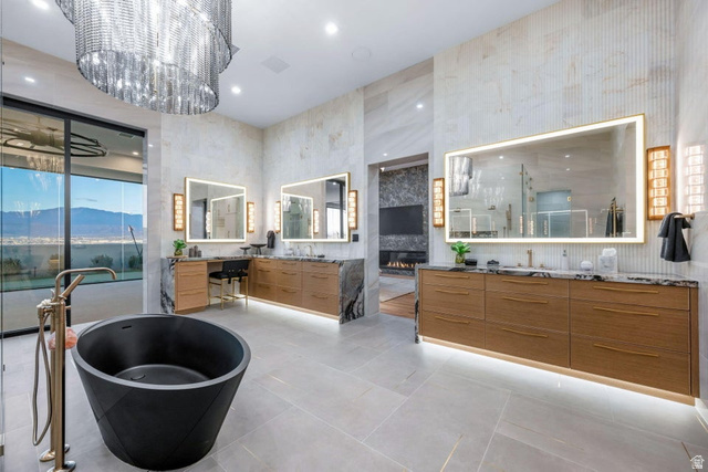 2867 East Granite Way St. George, UT 84790 - Photo 30 of 69 Spacious bathroom featuring a freestanding black soaking tub, dual floating wood-finish vanities with stone countertops, backlit mirrors, and a large multi-tiered chandelier