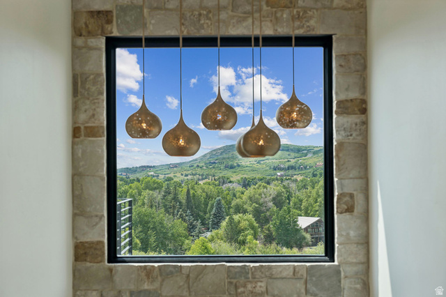 1400 Weber Wild Road Oakley, UT 84055 - Photo 10 of 55 Stone-framed window featuring a five-light pendant fixture, showcasing a mountain landscape with abundant trees and a clear sky