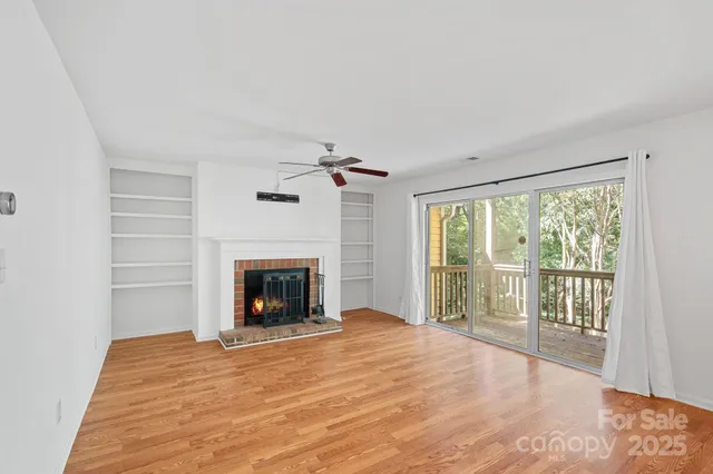 a view of an empty room with wooden floor fireplace and a window