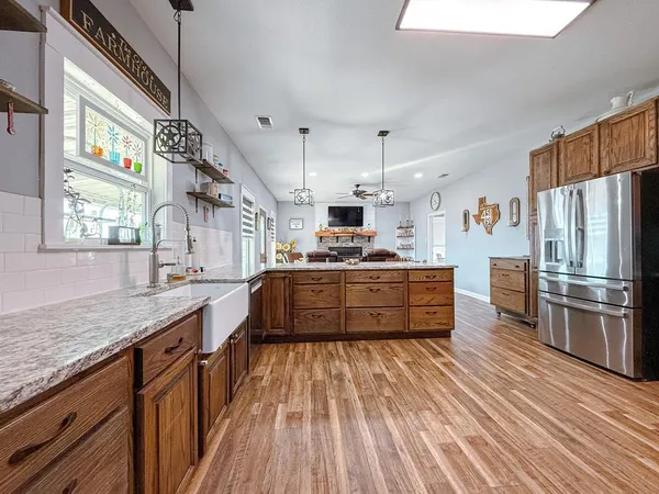 a kitchen with stainless steel appliances kitchen island granite countertop a refrigerator a stove a sink dishwasher and wooden cabinets with wooden floor