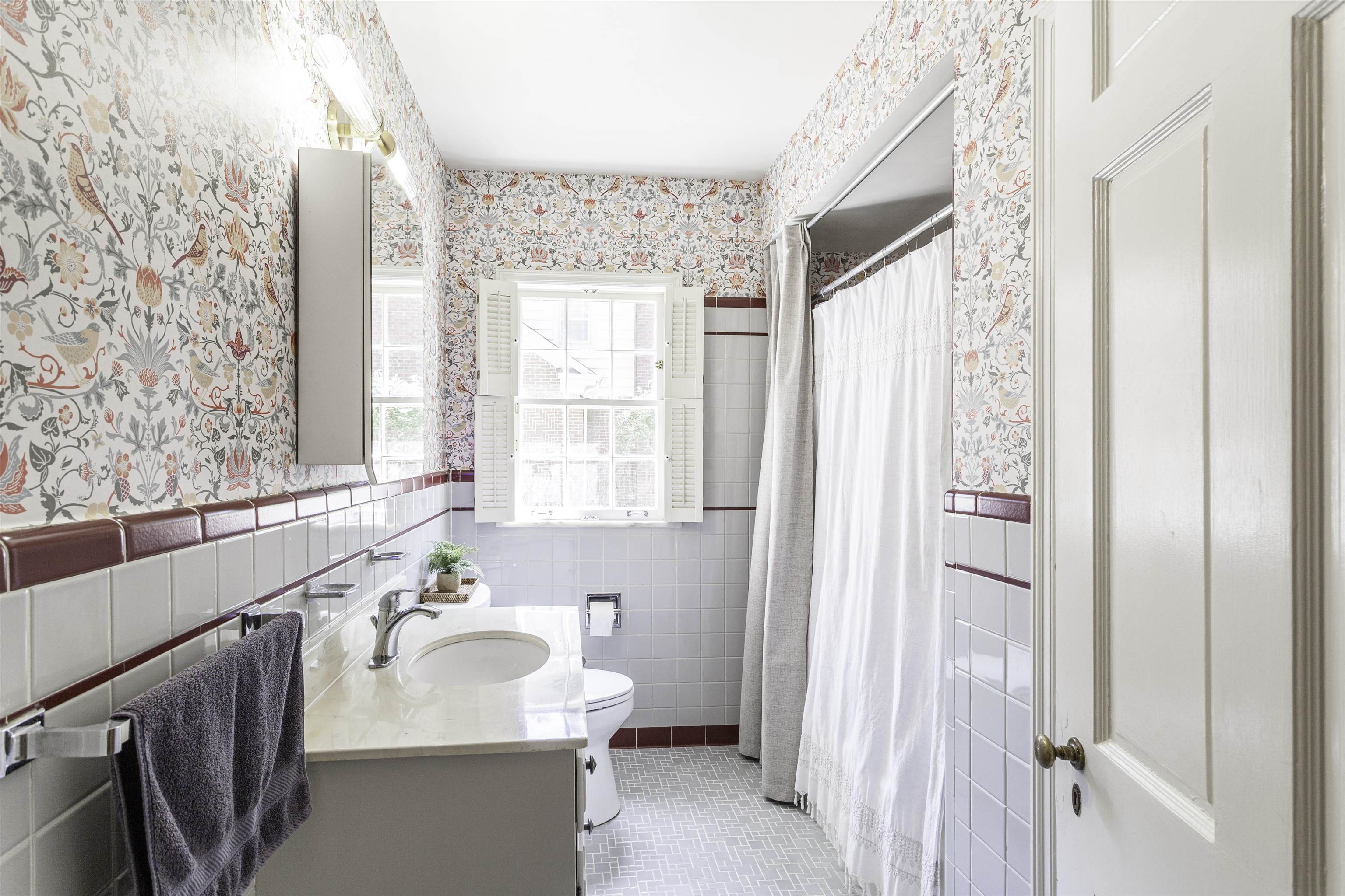 480 Colonial Road Memphis, TN 38117 - Photo 10 of 16 Bathroom featuring a vanity with an undermount sink and light-toned countertop, a window with white louvered shutters, a shower area with a curtain rod, white wall tiling with a brown accent border, and patterned wall covering
