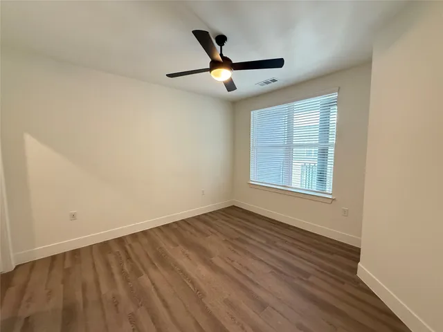 an empty room with wooden floor ceiling fan and windows