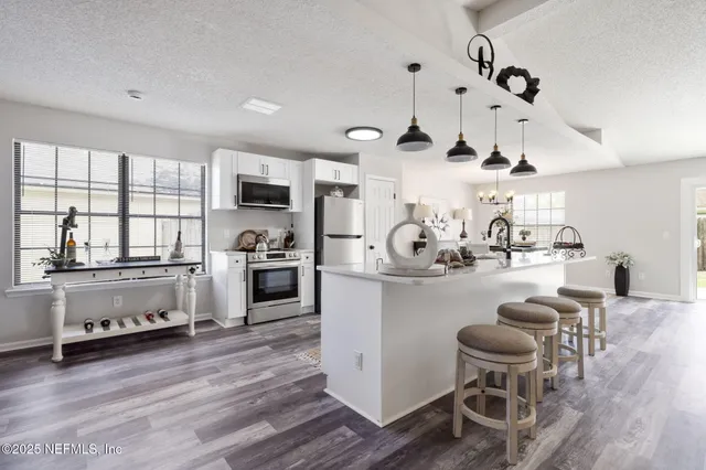 a kitchen with stainless steel appliances kitchen island granite countertop a stove a sink a refrigerator and white cabinets with wooden floor