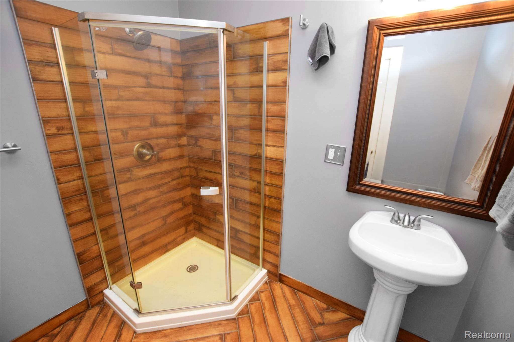 404 North Adelaide Street Fenton, MI 48430 - Photo 13 of 23 Corner glass shower enclosure with wood-finish tile surround, complemented by herringbone wood-finish flooring