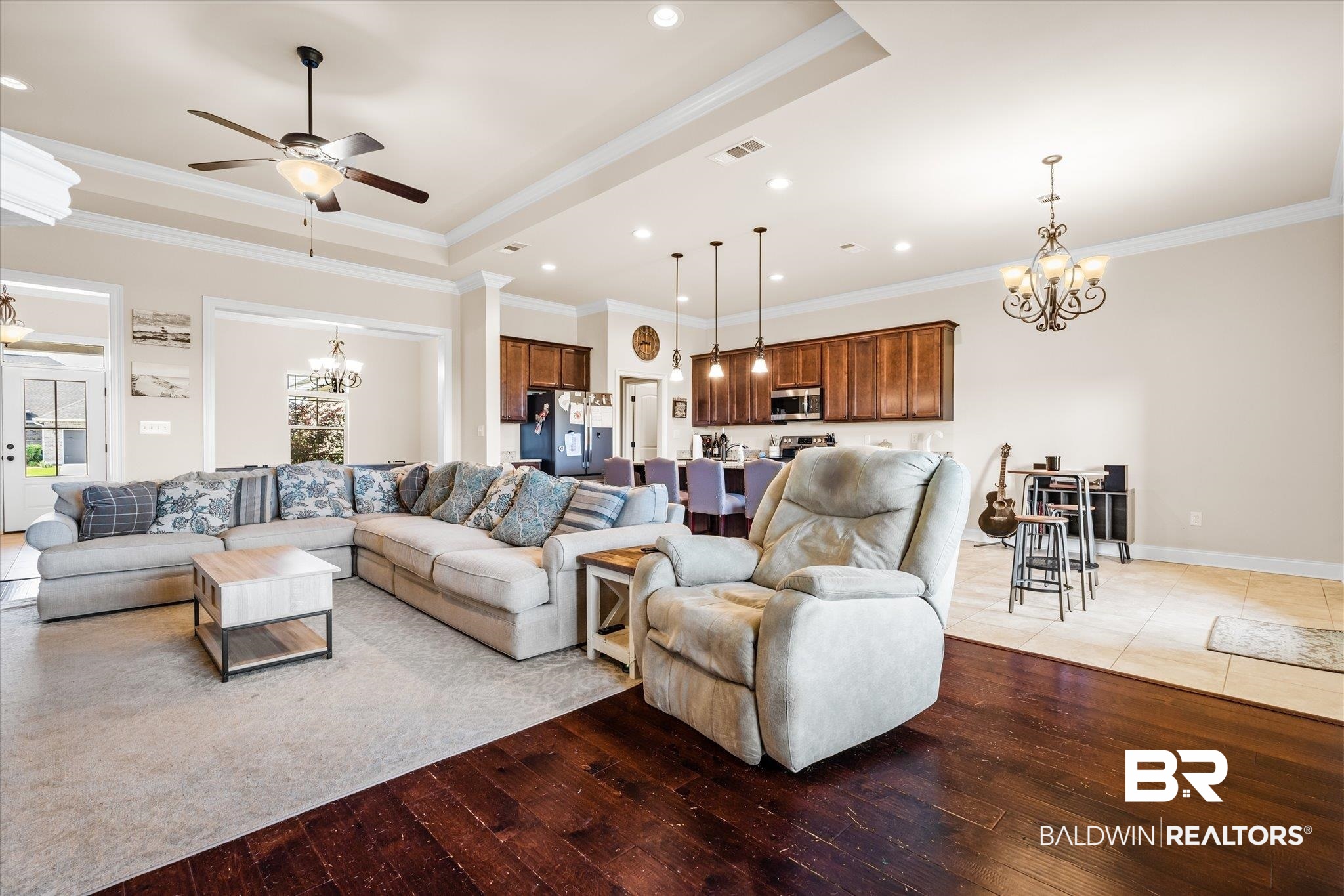 Living room with a chandelier, ornamental molding, light wood finished floors, a tray ceiling, and ceiling fan