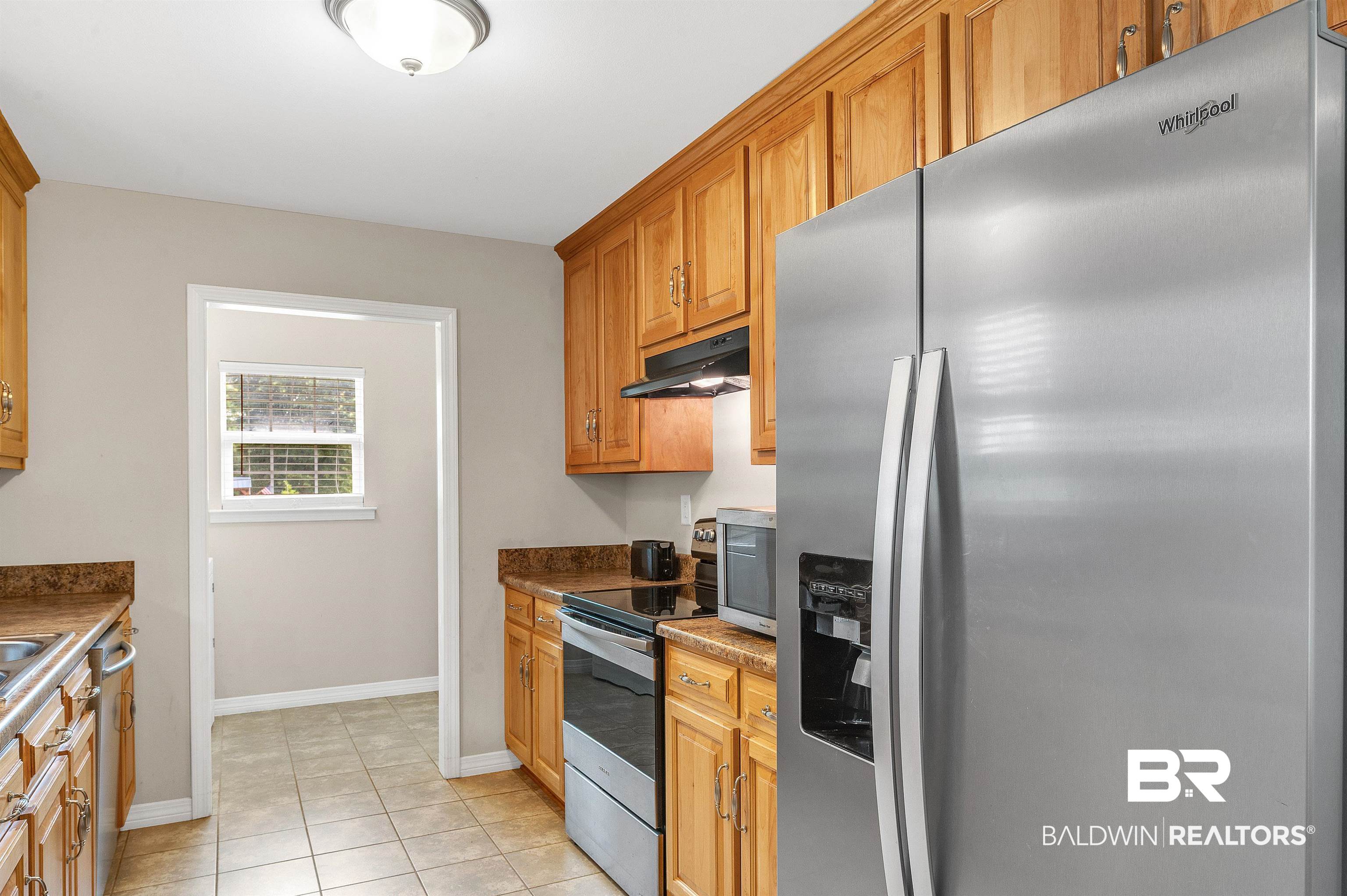 22810 Ard Road Robertsdale, AL 36567 - Photo 32 of 65 Kitchen with appliances with stainless steel finishes, under cabinet range hood, light tile patterned floors, brown cabinets, and dark countertops