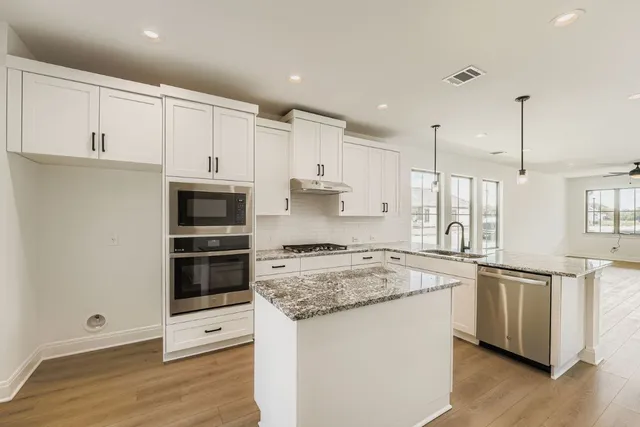 a kitchen with stainless steel appliances granite countertop a stove a sink and white cabinets