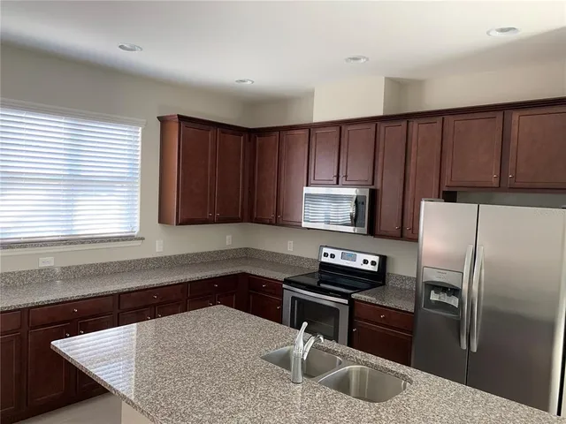 a kitchen with granite countertop a refrigerator a sink a stove a microwave and wooden cabinets