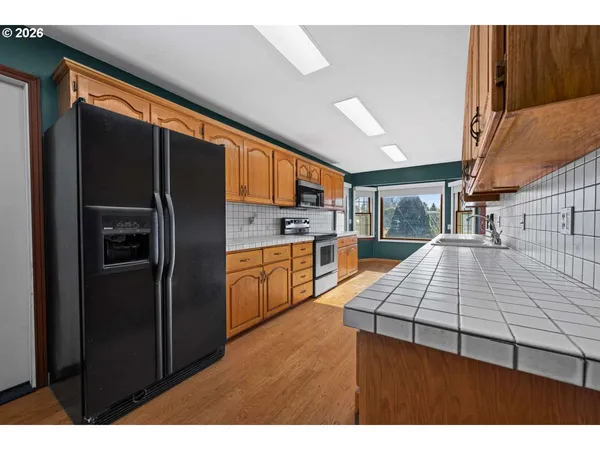 a kitchen with stainless steel appliances kitchen island granite countertop a refrigerator a stove and a sink with wooden cabinets