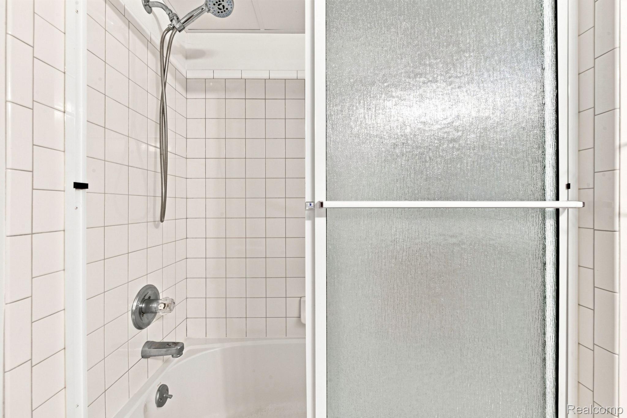 493 Harvard Drive Romeo, MI 48065 - Photo 24 of 36 Bathtub and shower combination featuring white square tile surround, chrome fixtures, and a textured glass shower door