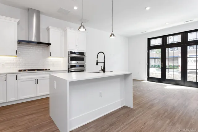 a kitchen with granite countertop a stove a sink a refrigerator and white cabinets with wooden floor