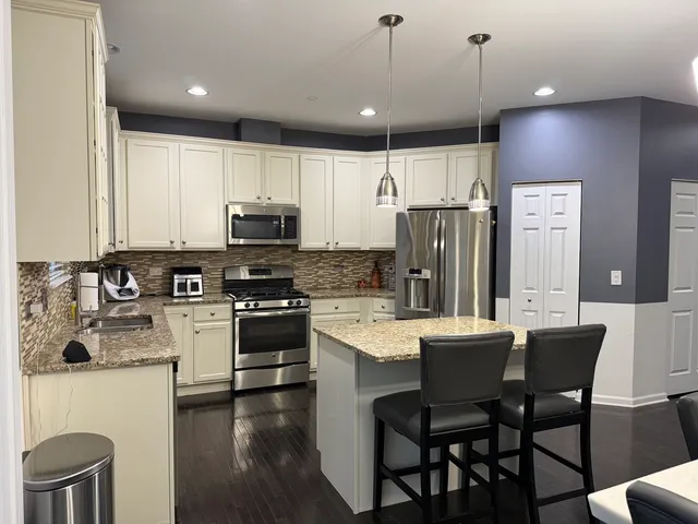 a kitchen with stainless steel appliances granite countertop a stove a sink a microwave a refrigerator with a dining table and chairs