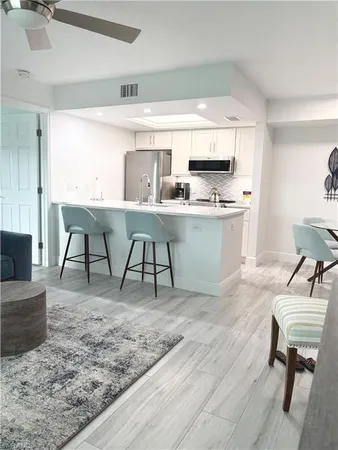 a living room with stainless steel appliances granite countertop a table chairs sink and cabinets