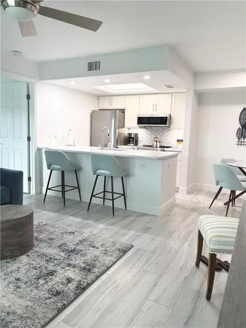 a living room with stainless steel appliances granite countertop a table chairs sink and cabinets
