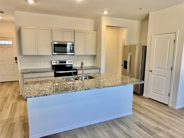 a kitchen with stainless steel appliances granite countertop a refrigerator a stove a sink and white cabinets with wooden floor