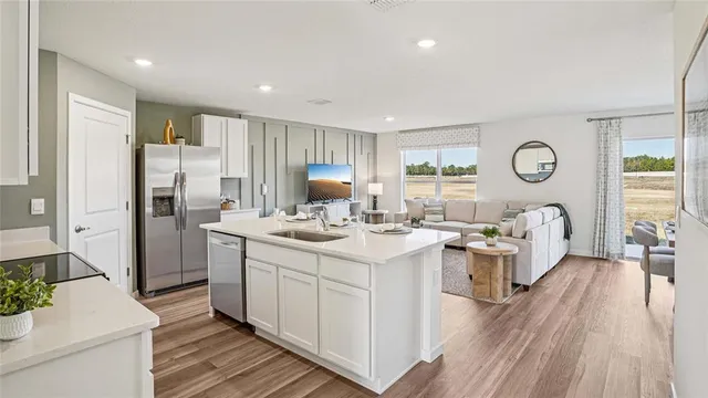 a large white kitchen with a lot of counter space a sink wooden floor and windows