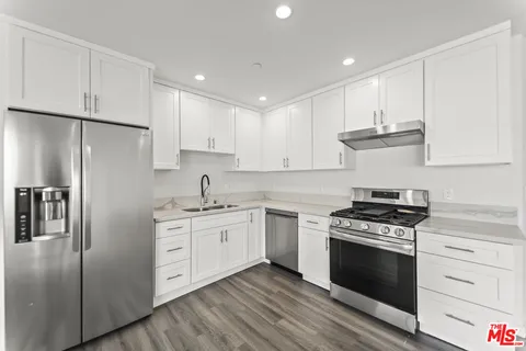 a kitchen with stainless steel appliances granite countertop a stove a refrigerator and a sink with wooden floor