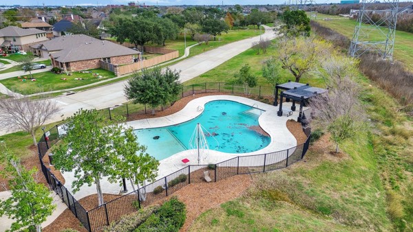2939 Canadian Goose Lane Baytown, TX 77521 - Photo 41 of 44 This photo showcases a community pool with a unique shape, surrounded by a fence and landscaped with trees. There's a shaded seating area nearby, and it is set in a residential neighborhood with nearby roads and houses.