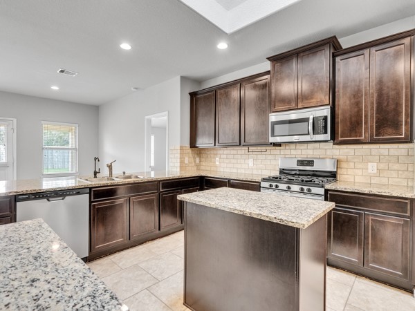 2939 Canadian Goose Lane Baytown, TX 77521 - Photo 6 of 44 This beautiful kitchen features dark wood cabinets, granite countertops, and stainless steel appliances, including a gas range and microwave. The space is well-lit with recessed lighting and a skylight. It also offers an open layout with a central island for additional prep space.