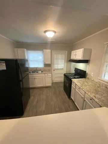 a kitchen with stainless steel appliances kitchen island granite countertop a refrigerator oven a sink dishwasher and white cabinets with wooden floor