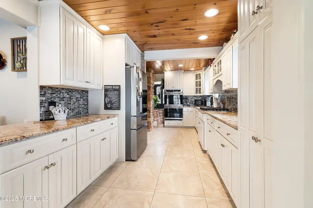 a large white kitchen with granite countertop a sink and dishwasher a stove with wooden cabinets