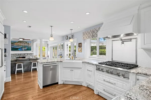 a kitchen with stainless steel appliances a stove a sink dishwasher and white cabinets with wooden floor