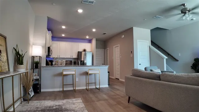 a living room with stainless steel appliances kitchen island granite countertop a refrigerator a stove and a sink with wooden floor