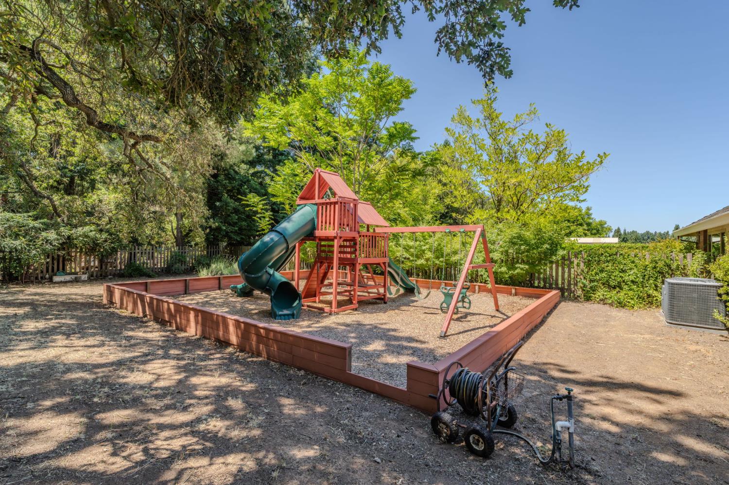 9069 Bader Road Elk Grove, CA 95624 - Photo 63 of 70 Outdoor play structure featuring a slide, swings, and climbing elements within a contained wood-edged area