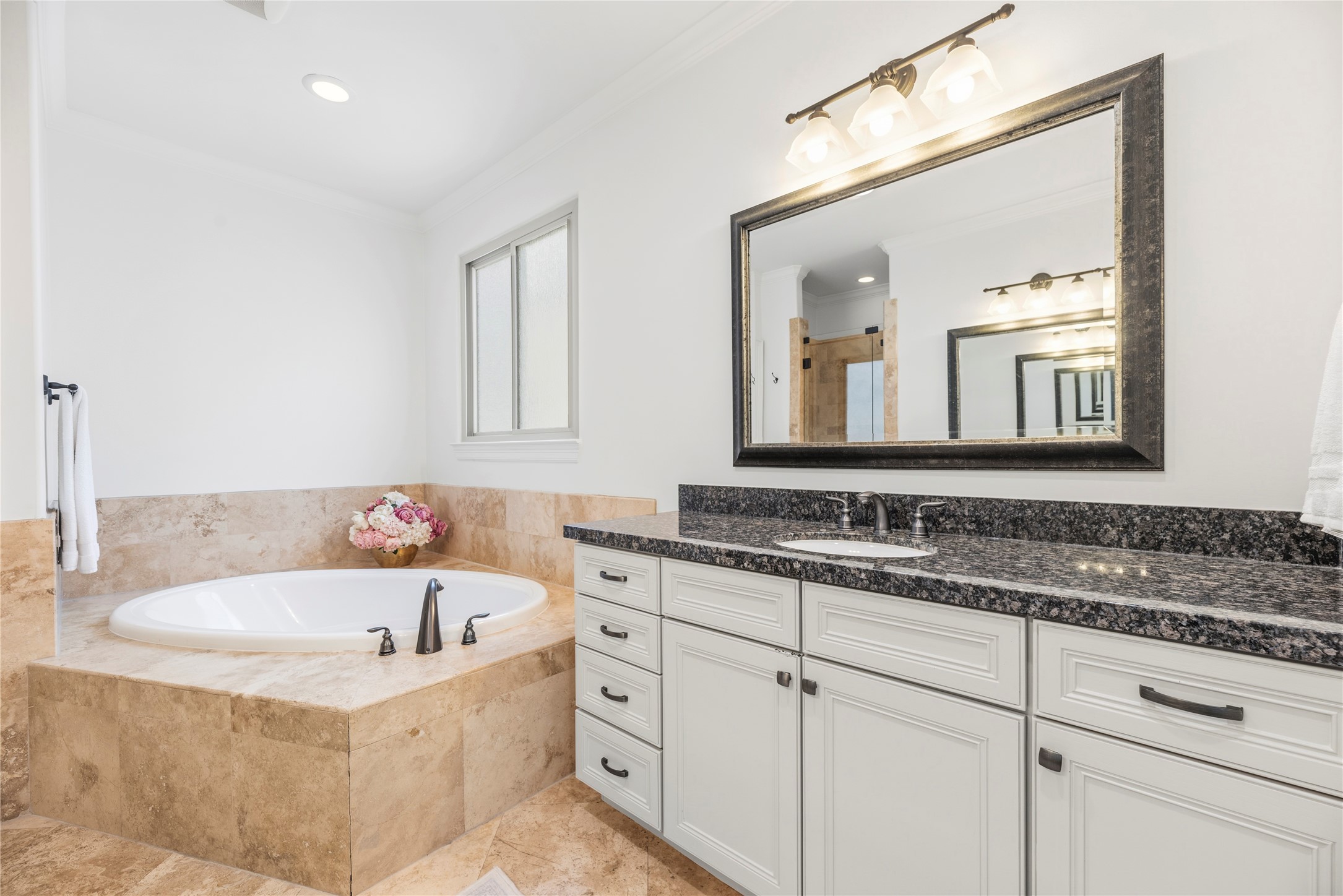 1537 Haddon Street Houston, TX 77006 - Photo 22 of 48 Primary bathroom features a luxurious corner bathtub with elegant stone tile surround, a large mirror above a granite-topped one of the vanities, and soft lighting, creating a serene and stylish space.