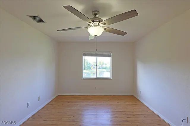 an empty room with wooden floor chandelier fan and windows