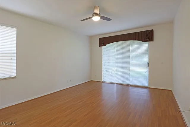 an empty room with wooden floor chandelier fan and windows