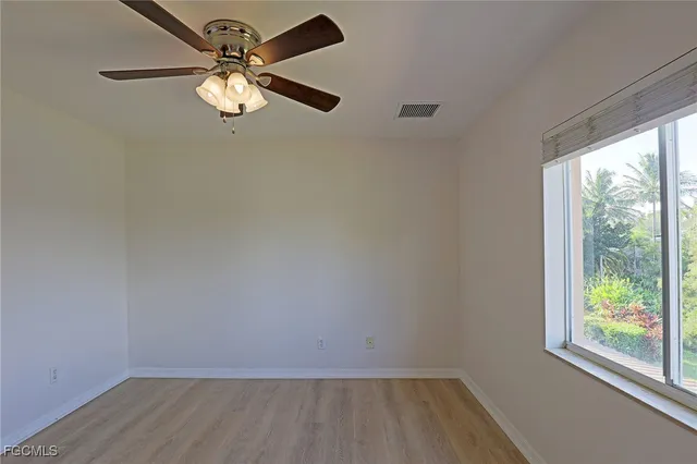 an empty room with wooden floor fan and windows