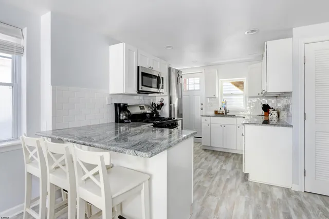 a kitchen with stainless steel appliances granite countertop a stove a sink a microwave a refrigerator and white cabinets with wooden floor