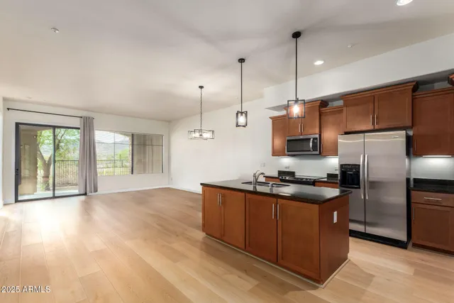 a kitchen with stainless steel appliances granite countertop a stove a refrigerator a sink a dining table and chairs with wooden floor